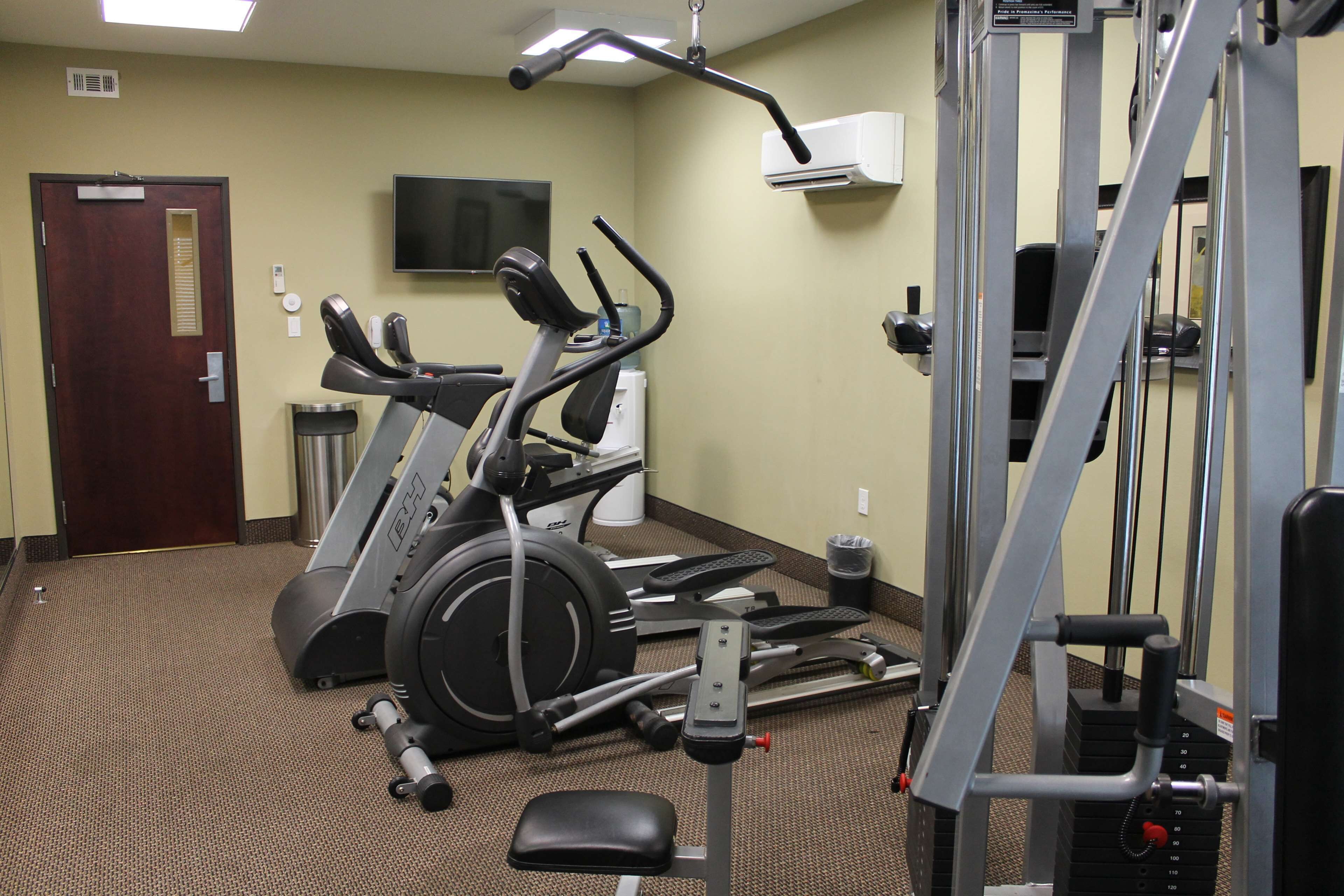 A gym with exercise equipment, a television on the wall, and a door.
