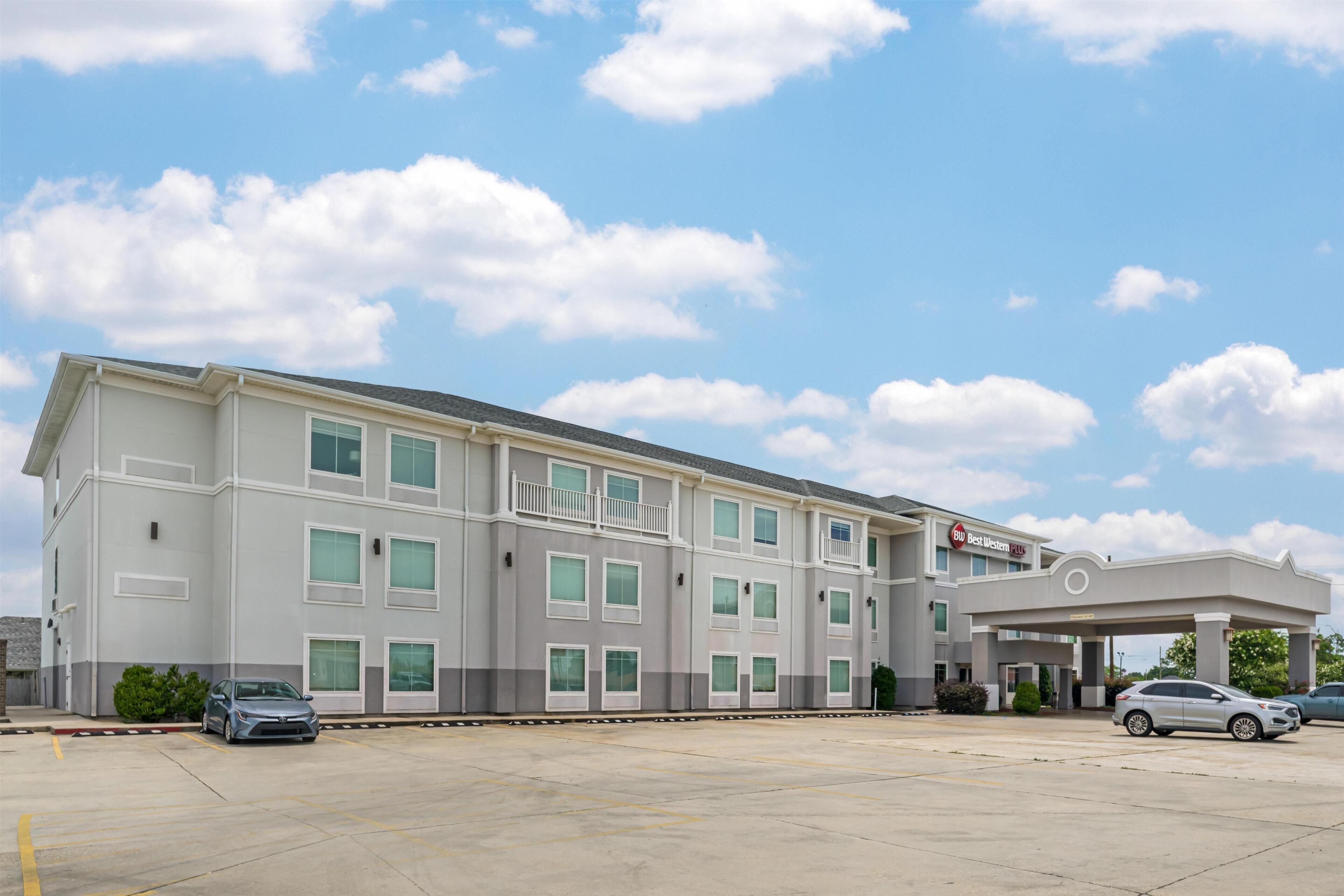 A multi-story hotel with a gas station attached, featuring a large parking lot and several cars parked.