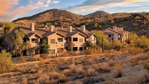 A residential area with multiple houses featuring similar architectural styles, surrounded by dry, rocky terrain and sparse vegetation. - Raintree at Phoenix South Mountain Preserve (Phoenix)