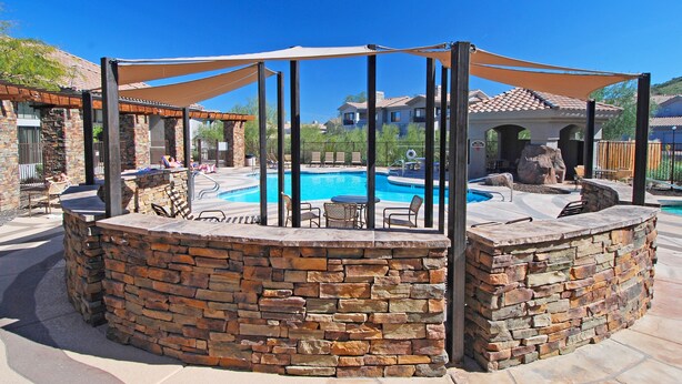 A stone poolside area with a covered seating area and a stone wall. - Raintree at Phoenix South Mountain Preserve (Phoenix)