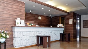 A reception area with a stone counter, wooden paneling, and a clock. - Hotel Route-Inn Court Minami Alps (Minami-Alps)