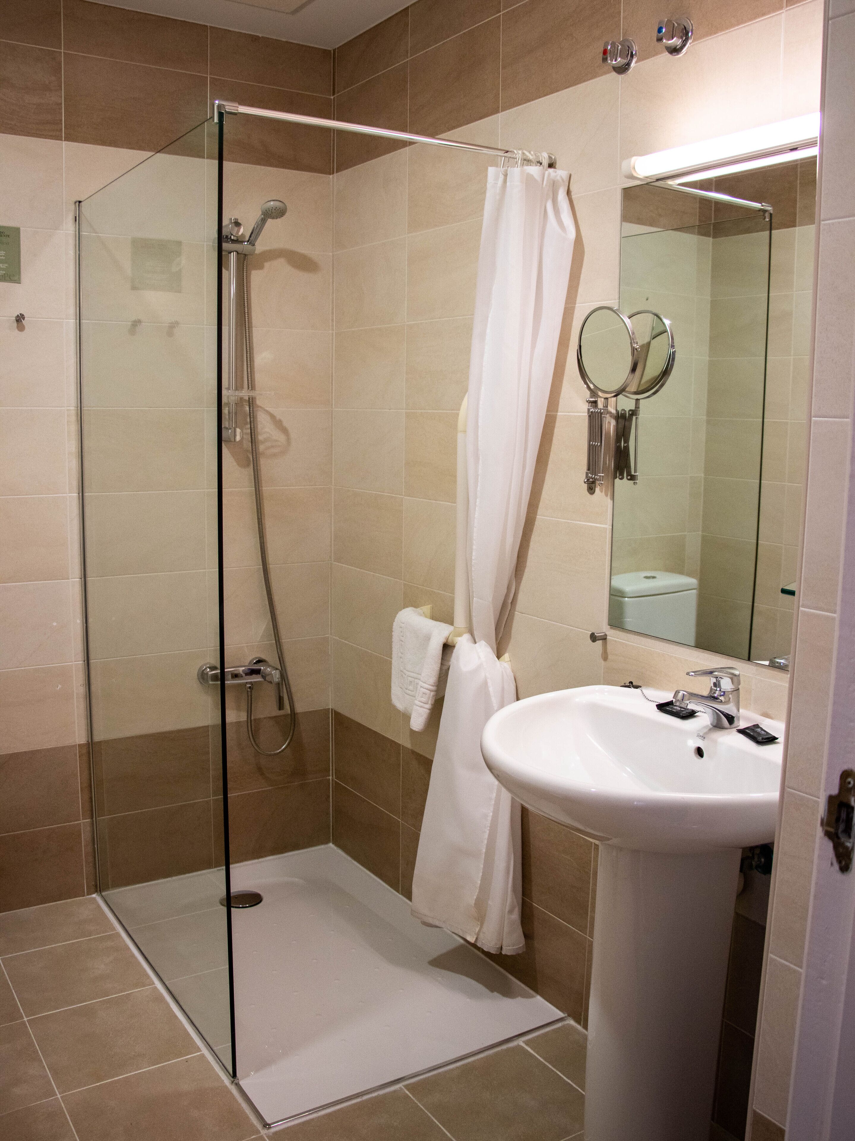 A modern bathroom with a glass-enclosed shower, a white sink, and a large mirror.