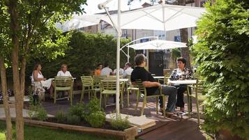 Un patio al aire libre con sillas y mesas verdes bajo sombrillas blancas, rodeado de follaje y árboles.