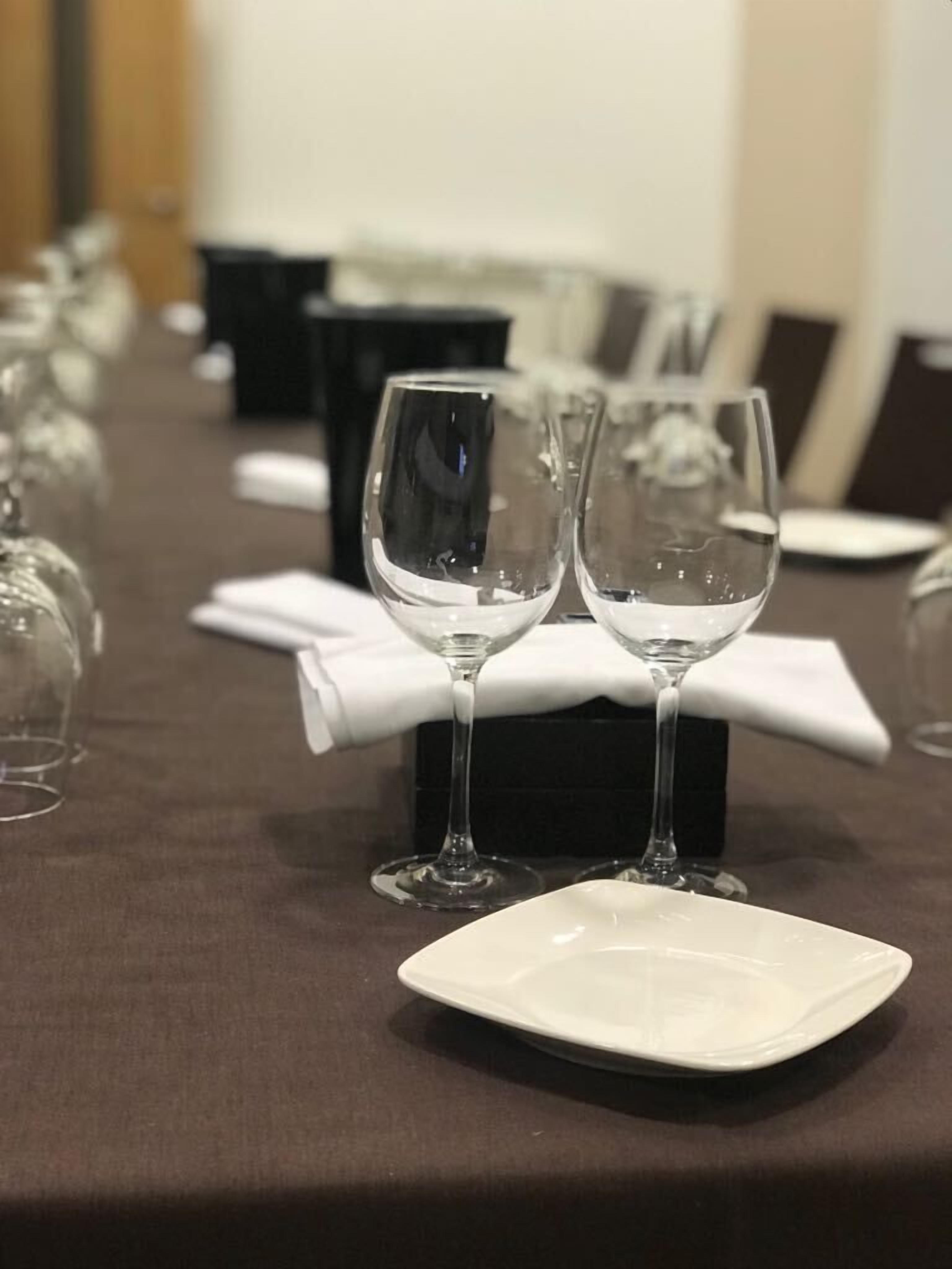 Una mesa con copas de vino y un plato blanco, con una caja negra y una servilleta blanca sobre la mesa.
