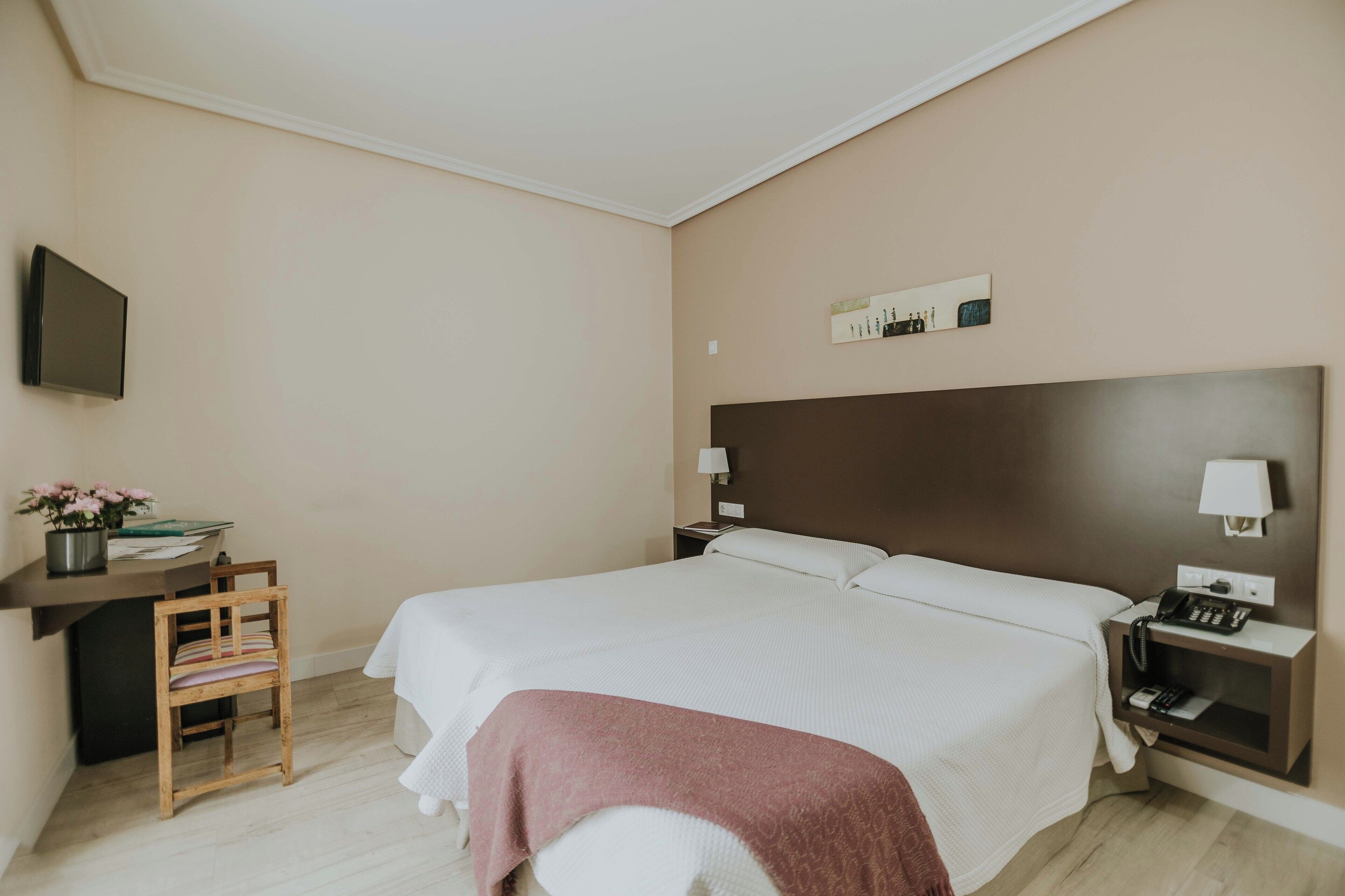 Habitación de hotel con una cama grande, un escritorio con silla, un televisor y una mesita de noche con lámpara.