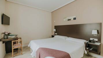 Habitación de hotel con una cama grande, un escritorio con silla, un televisor y una mesita de noche con lámpara.