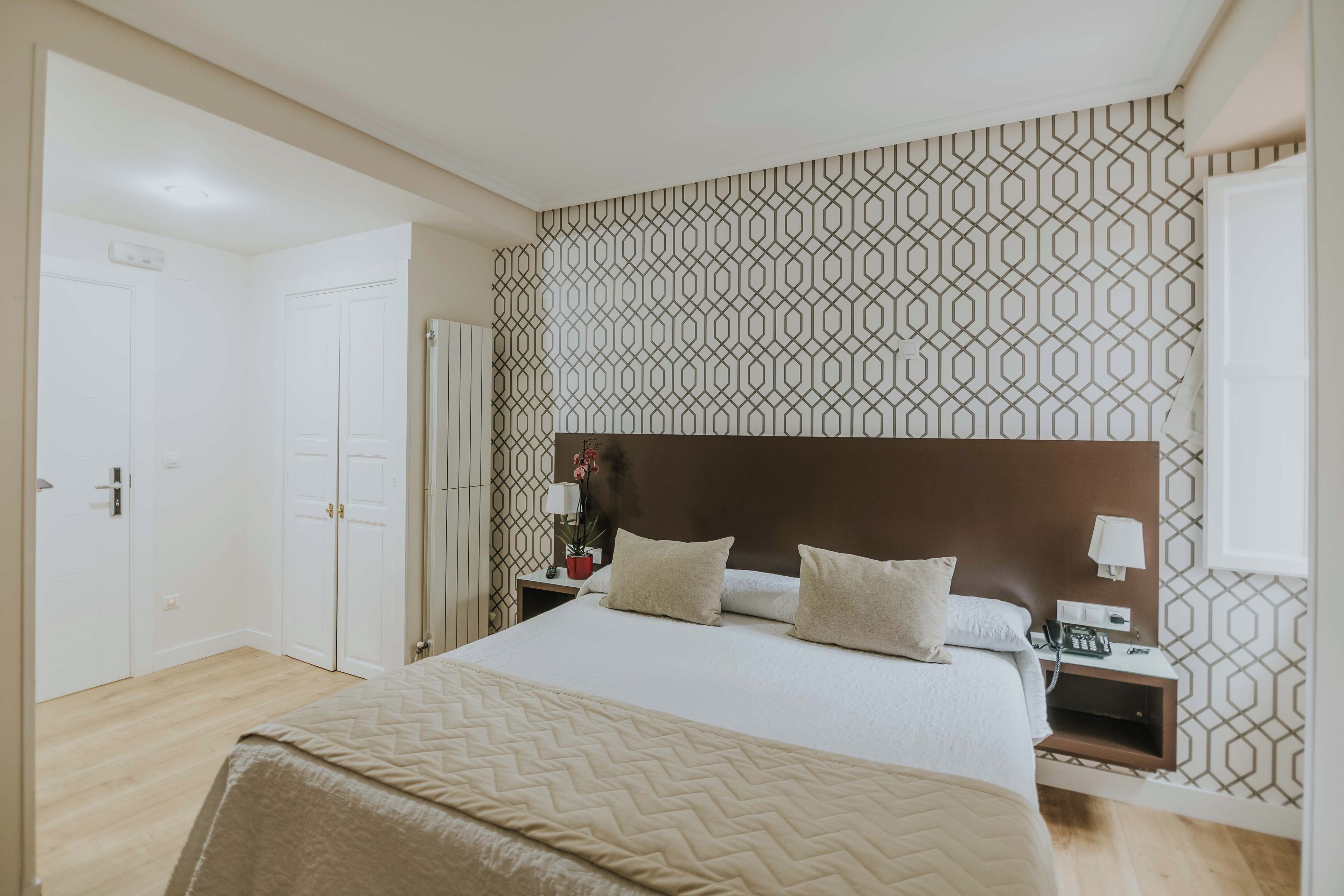 A hotel room with a large bed, bedside tables, a nightstand, a lamp, a telephone, and a patterned wall.