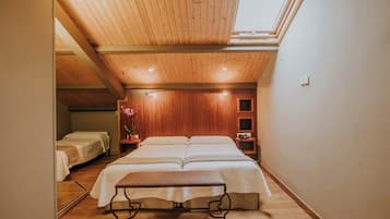 A bedroom with a wooden ceiling, a skylight, a large bed, bedside tables, and a small bedside lamp.