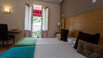 Quarto de hotel com duas camas, uma escrivaninha com cadeira, mesa de cabeceira e janela com porta aberta.