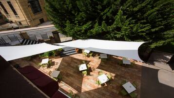 An outdoor patio area with tables and chairs, surrounded by a building and a large tree.