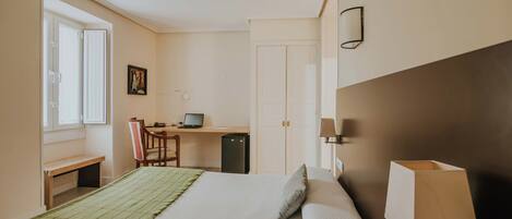 Habitación de hotel con cama, escritorio, laptop, silla, mesita y lámpara.