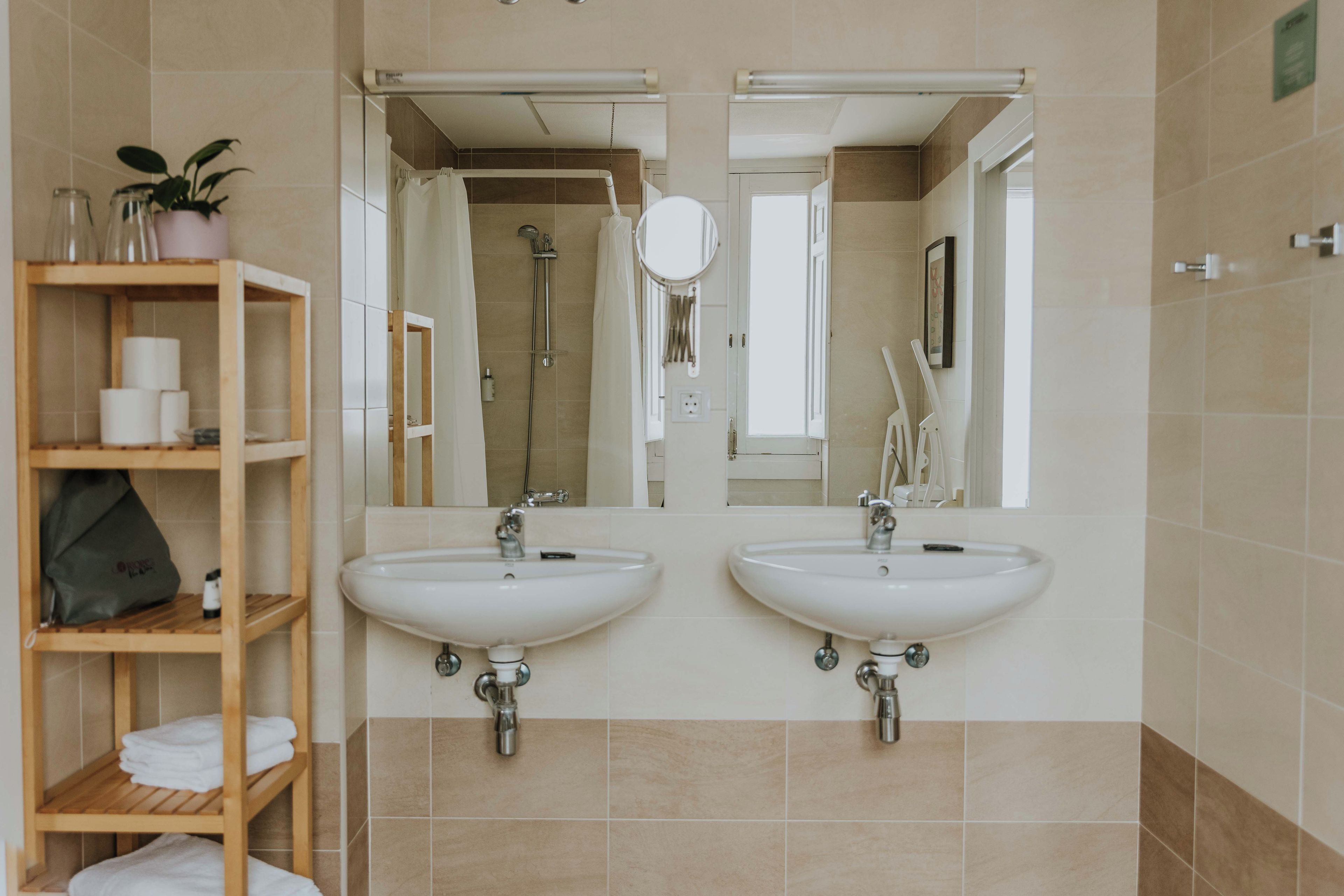 Une salle de bain avec deux lavabos, une douche, un miroir et une étagère où sont rangées les serviettes et les articles de toilette.