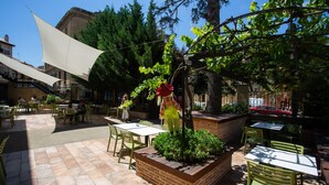 An outdoor patio area with tables and chairs, surrounded by greenery and trees. - Hotel Arrope (Haro)