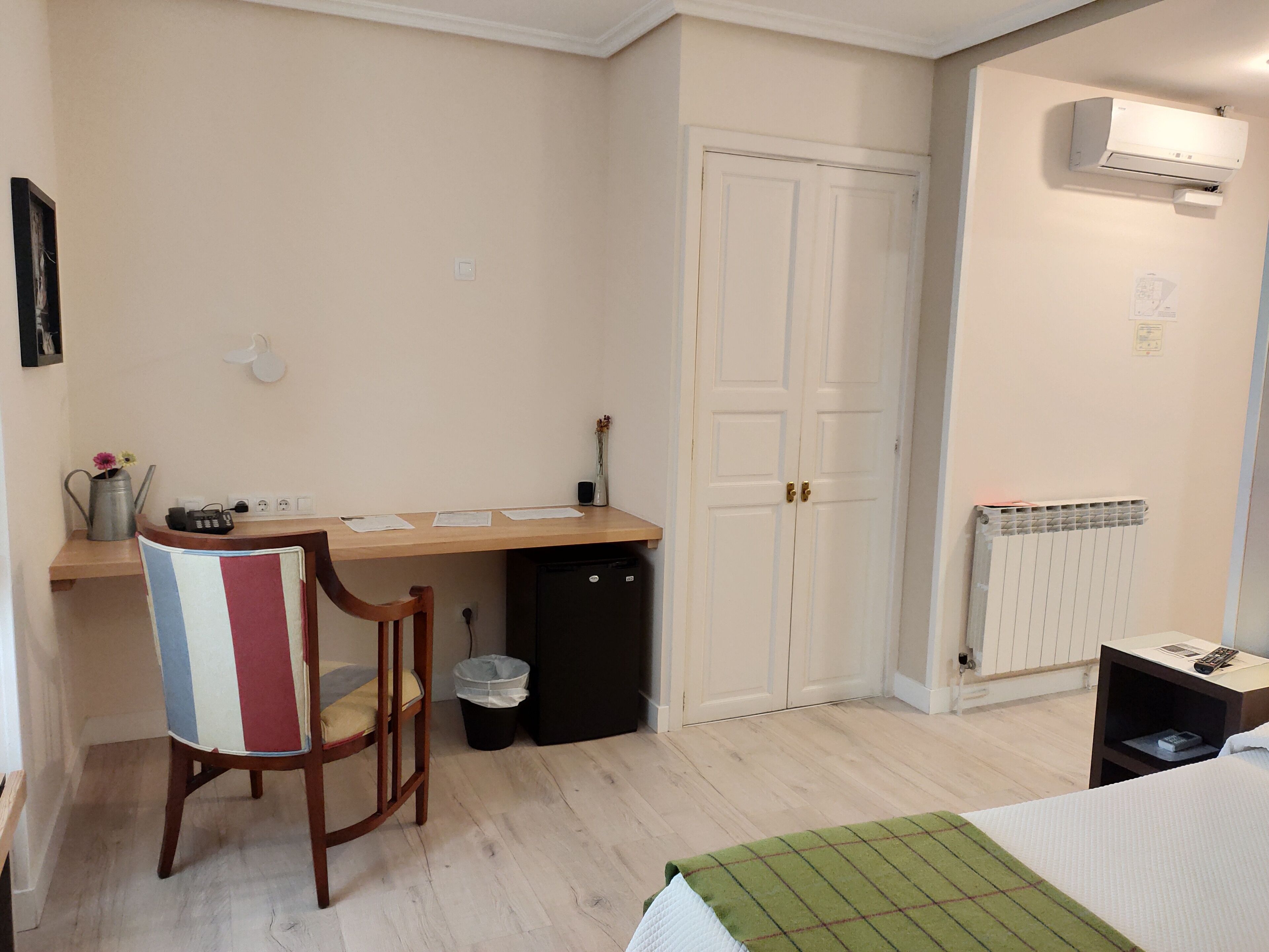 A small, tidy room with a wooden desk, a chair, a radiator, and a bed.