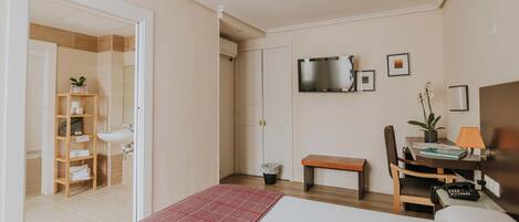 Quarto de hotel com uma cama, uma secretária com cadeira, televisão e banheiro visível por uma porta aberta.