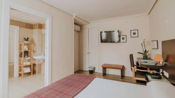 A hotel room with a bed, a desk with a chair, a TV, and a bathroom visible through an open door.