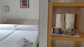 Ein Hotelzimmer mit zwei Betten, einem Holzboden mit Handtüchern und Toilettenartikeln, einem gerahmten Bild an der Wand und einer Deckenleuchte.