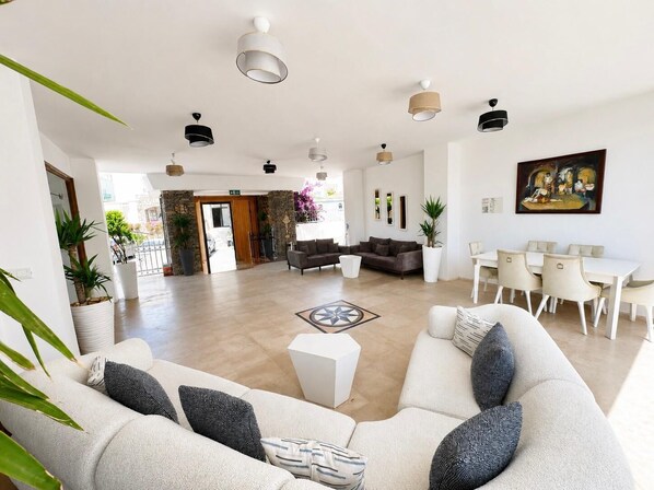 A spacious lobby with a sofa, dining area, and potted plants.
