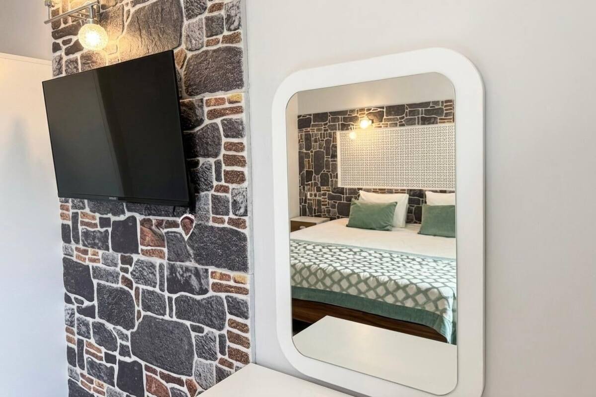 Ein Zimmer mit einer Steinsäule, einem an der Wand befestigten Fernseher und einem Spiegel, der ein Bett mit einem gemusterten Überwurf zeigt.