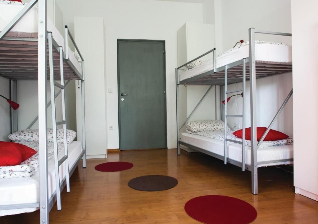 Um dormitório com beliches, uma porta e três tapetes redondos no chão.