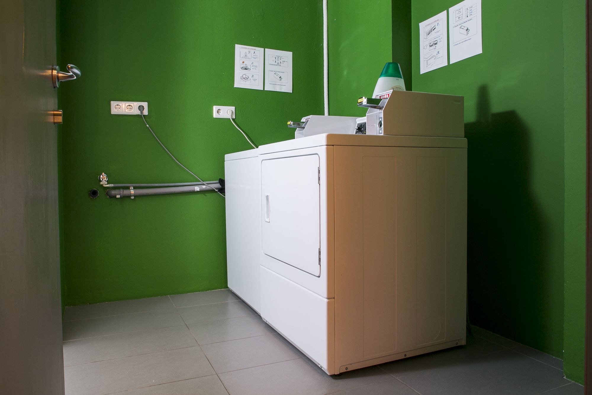 A compact laundry area with a white washing machine, a green wall, and instructional posters.