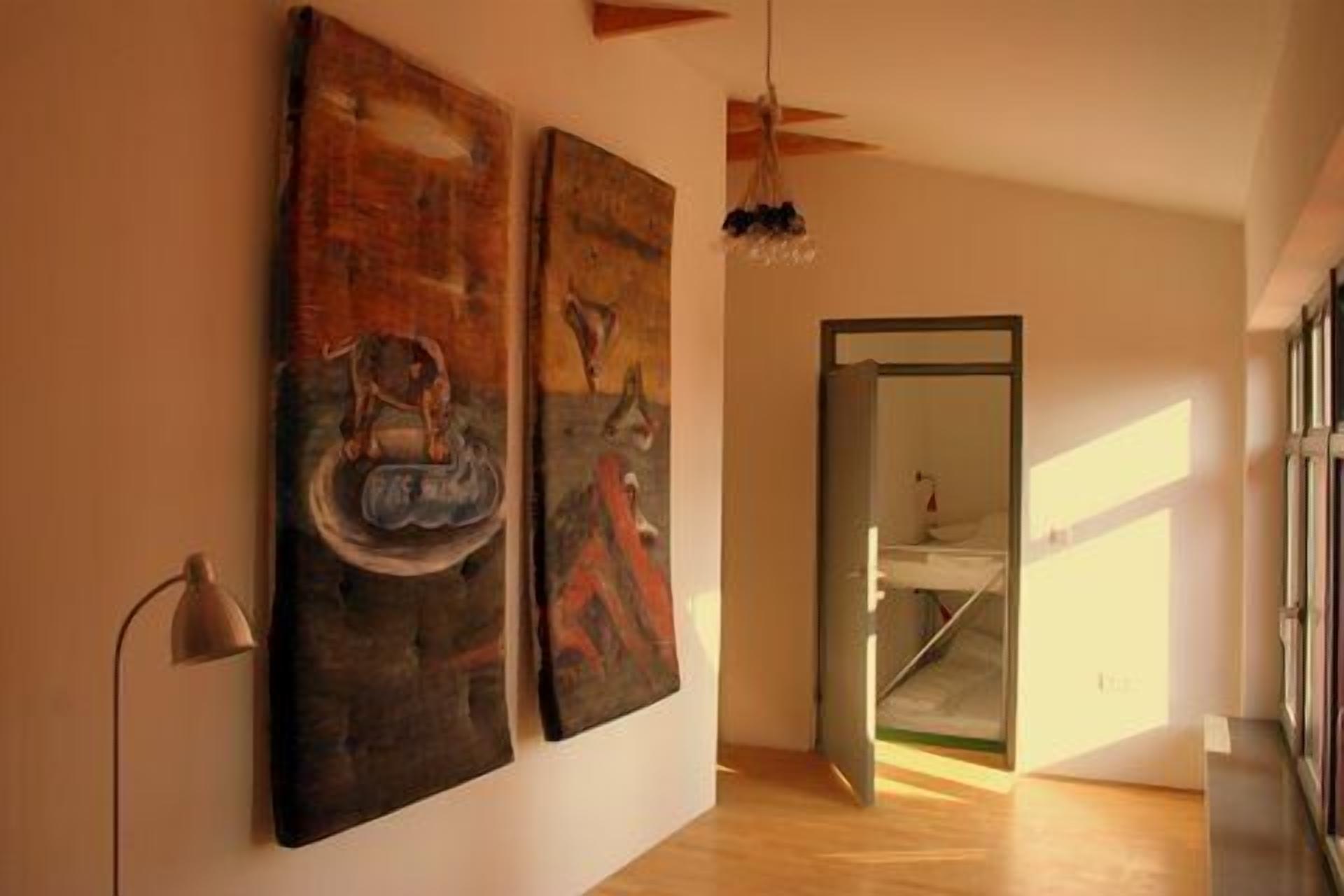 A hallway with two large abstract paintings on the wall, a ceiling fan, and a door leading to another room.