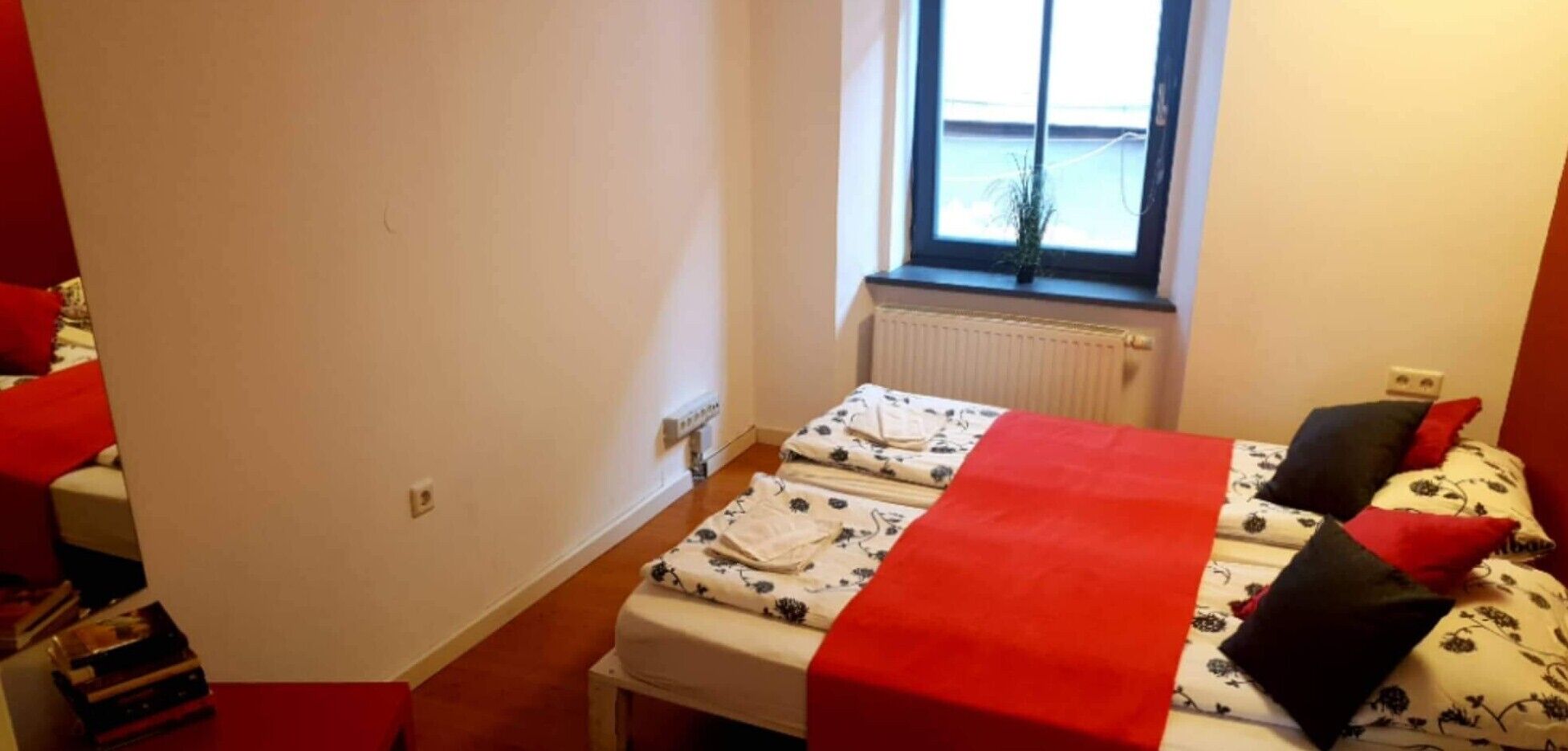 Een kleine, compacte kamer met twee bedden, een radiator en een raam met uitzicht.