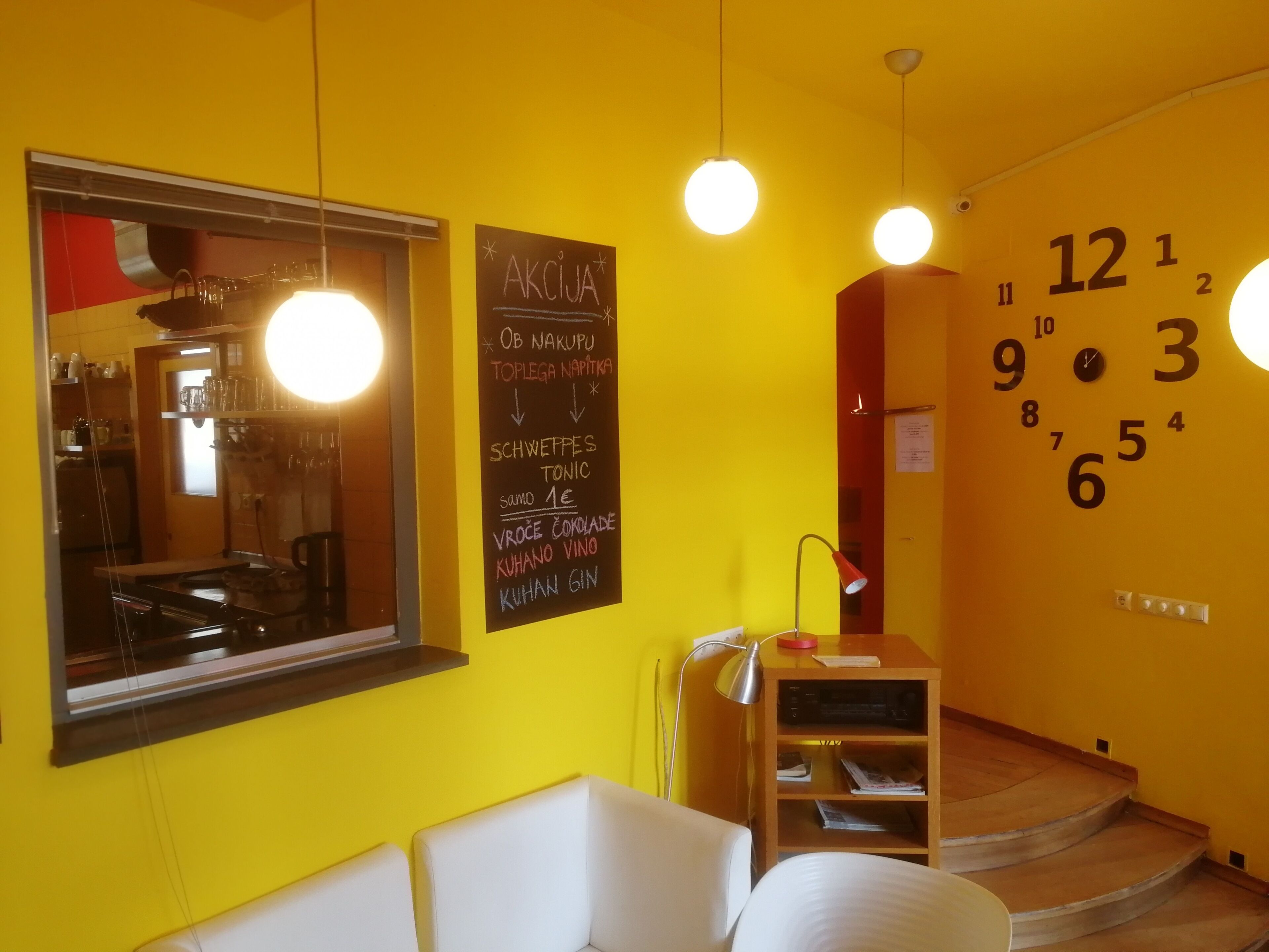 Una habitación con una pared amarilla, un menú en pizarra, un reloj y una ventana.