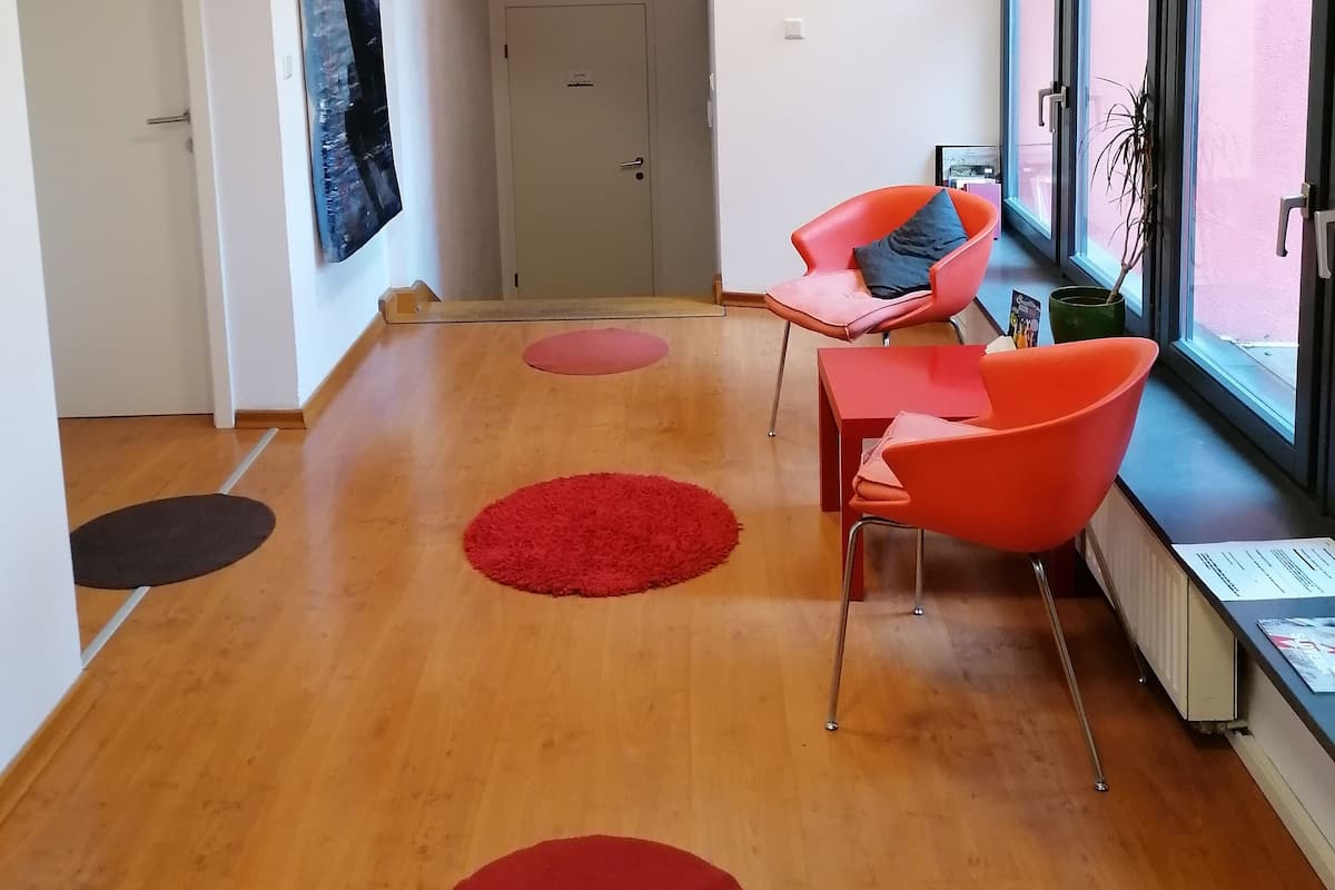 Uma sala de estar moderna com piso de madeira, tapetes circulares vermelhos, uma poltrona vermelha e uma janela com vista.
