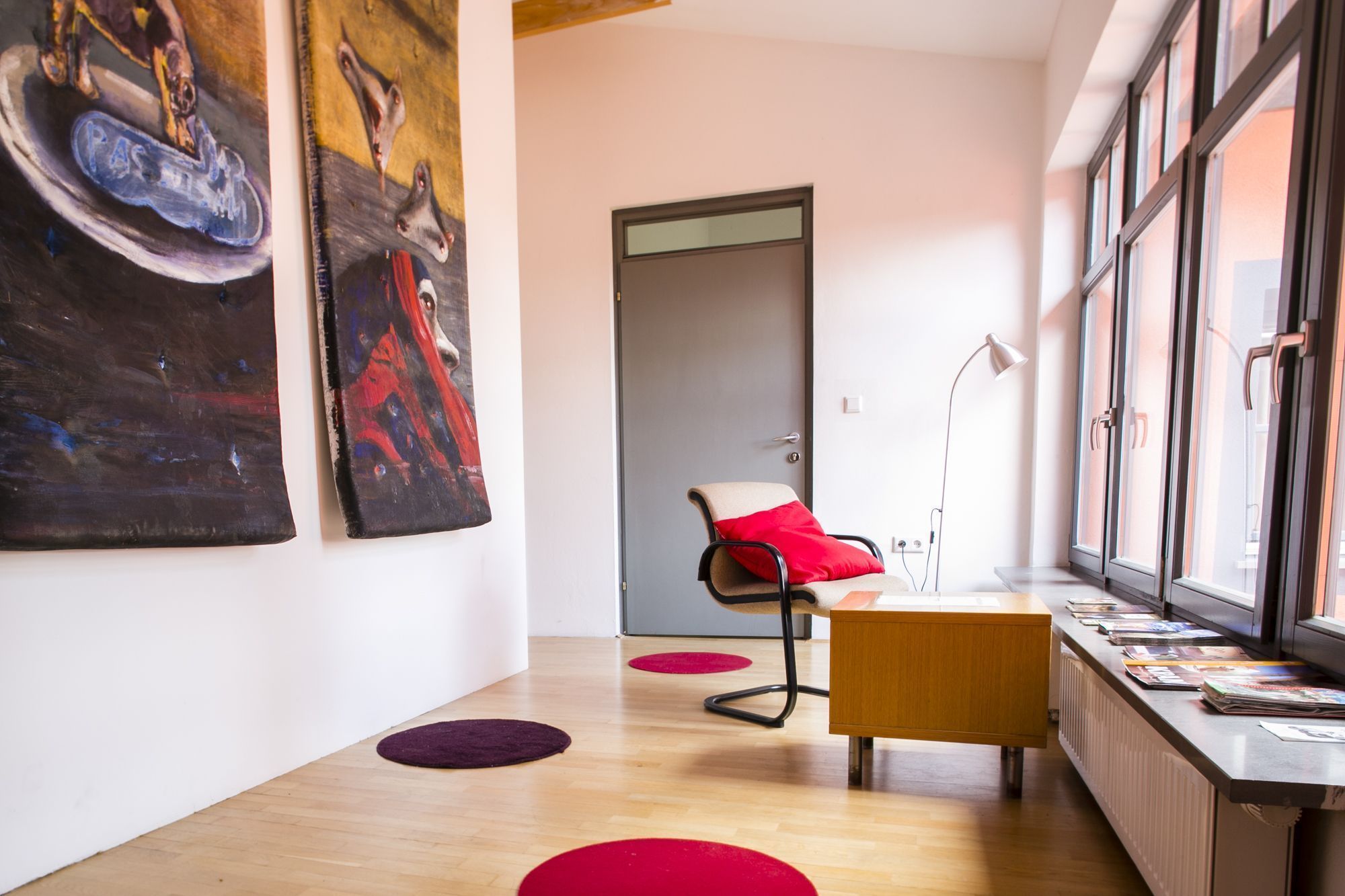 Un interior moderno con suelo de madera, una silla roja, una mesita de madera y una estantería con libros.