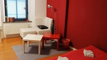 A bedroom with a bed, a desk, a chair, a radiator, a window with blinds, and a red wall.