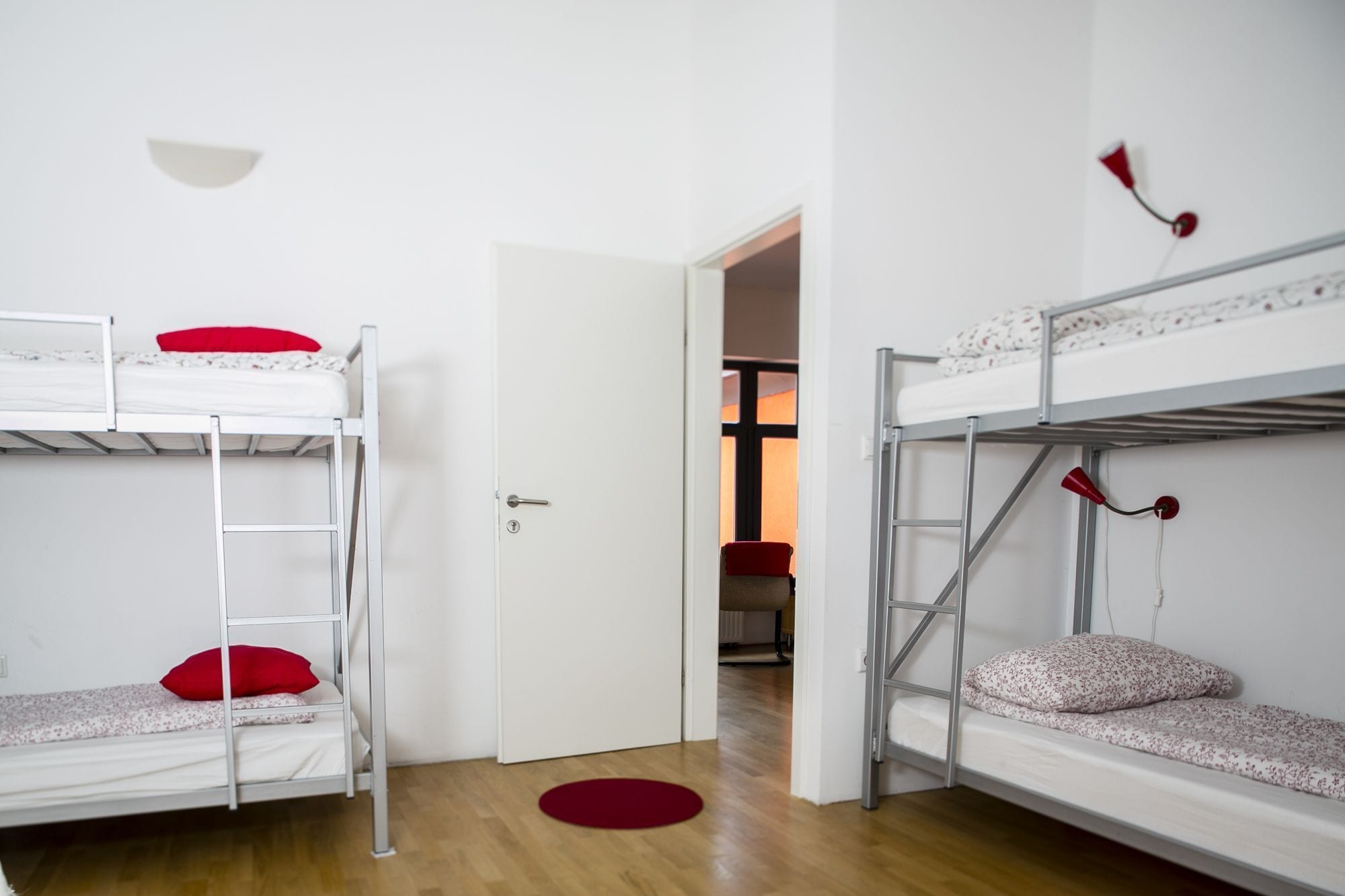 A room with two bunk beds, a door leading to another room, and a red rug on the floor.