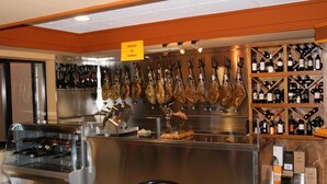 A restaurant with a display of cured meats, a wine rack, and a glass display case with bottles. - Hotel Alameda (Alba de Tormes)