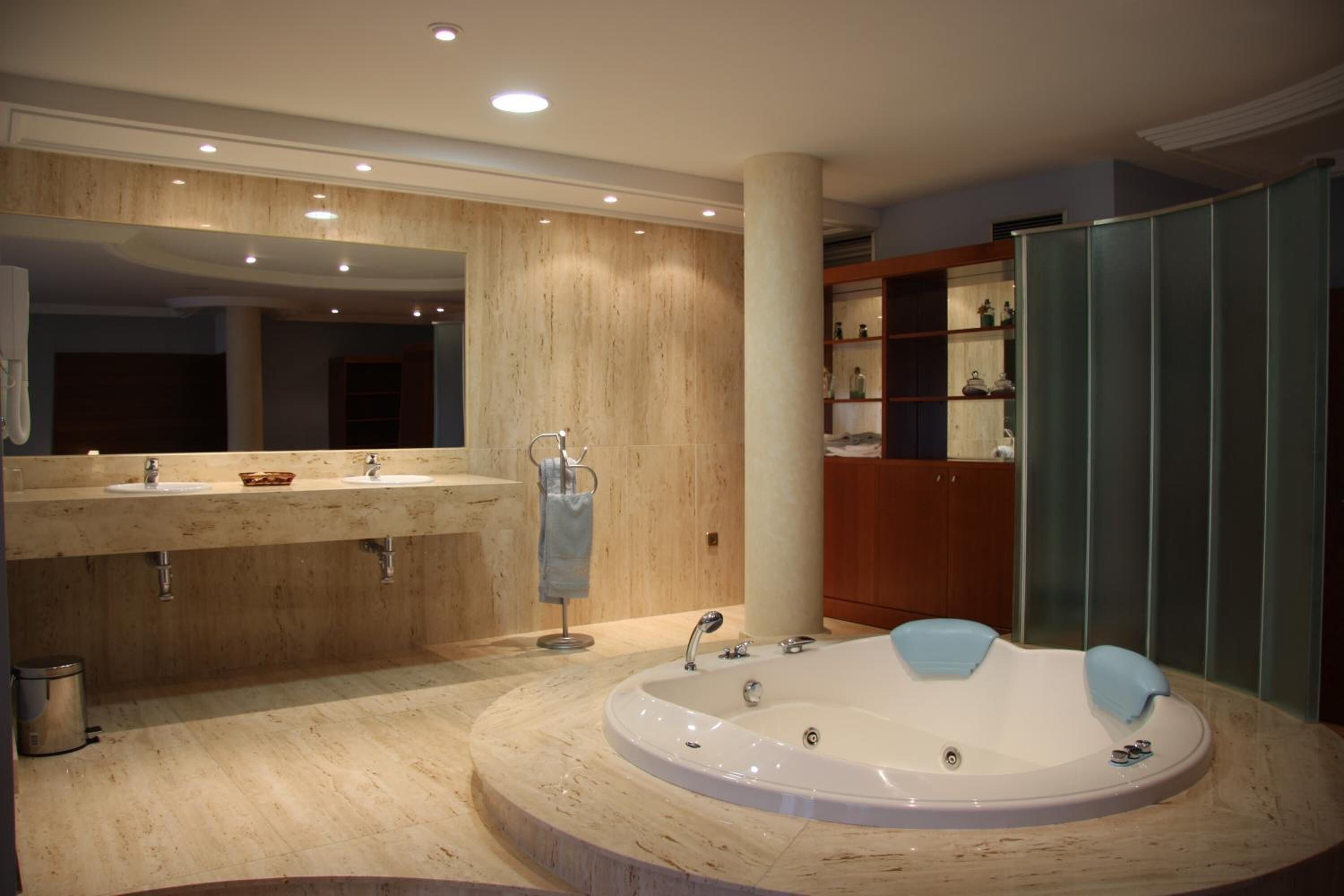 A modern bathroom with a large mirror, two sinks, a bathtub, and a wooden vanity.