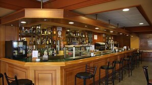 A bar area with a counter, stools, and shelves of bottles. - Hotel Alameda (Alba de Tormes)