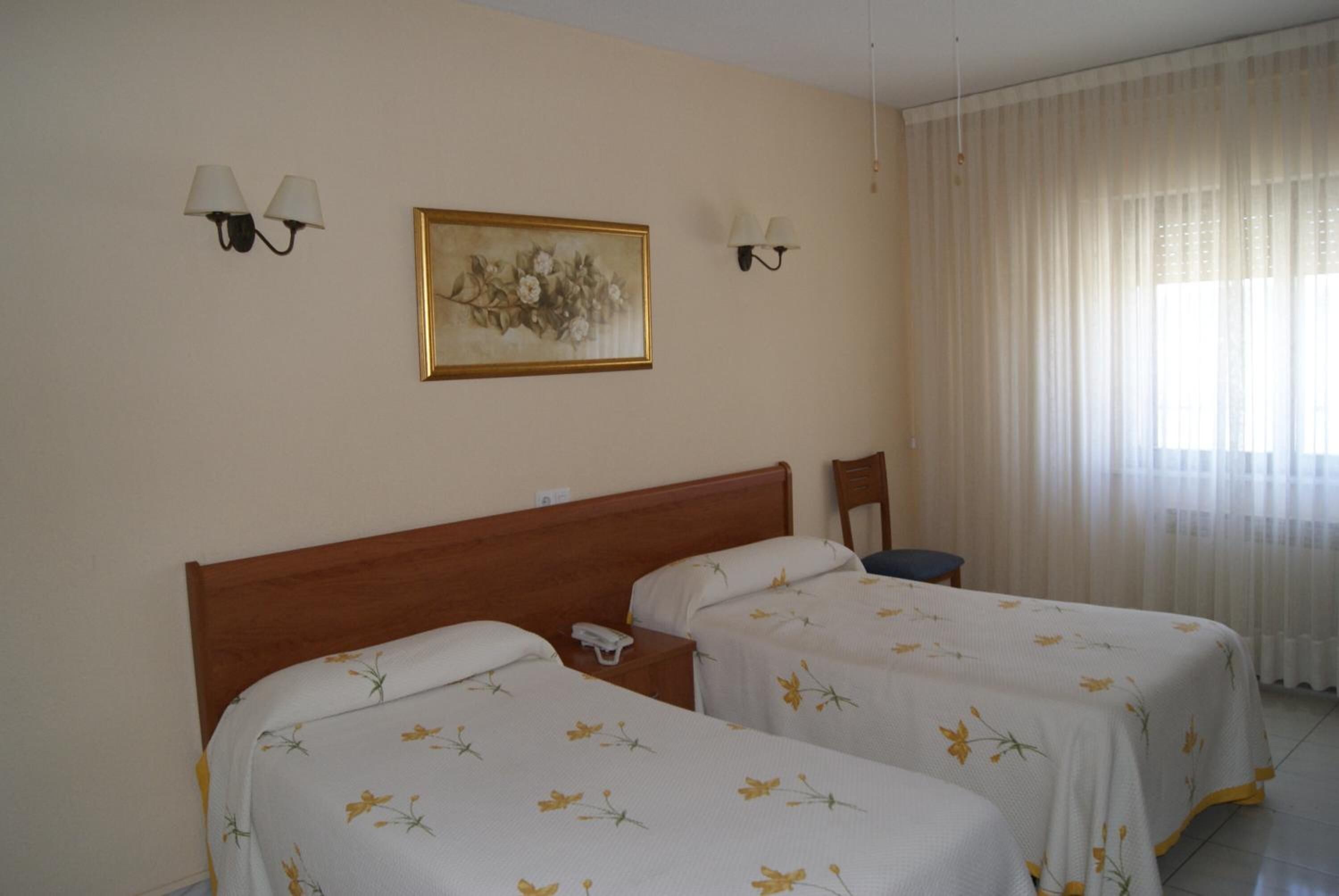 A hotel room with two single beds, a wooden headboard, a nightstand with a phone, and a painting on the wall.