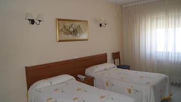 A hotel room with two single beds, a wooden headboard, a nightstand with a phone, and a painting on the wall.