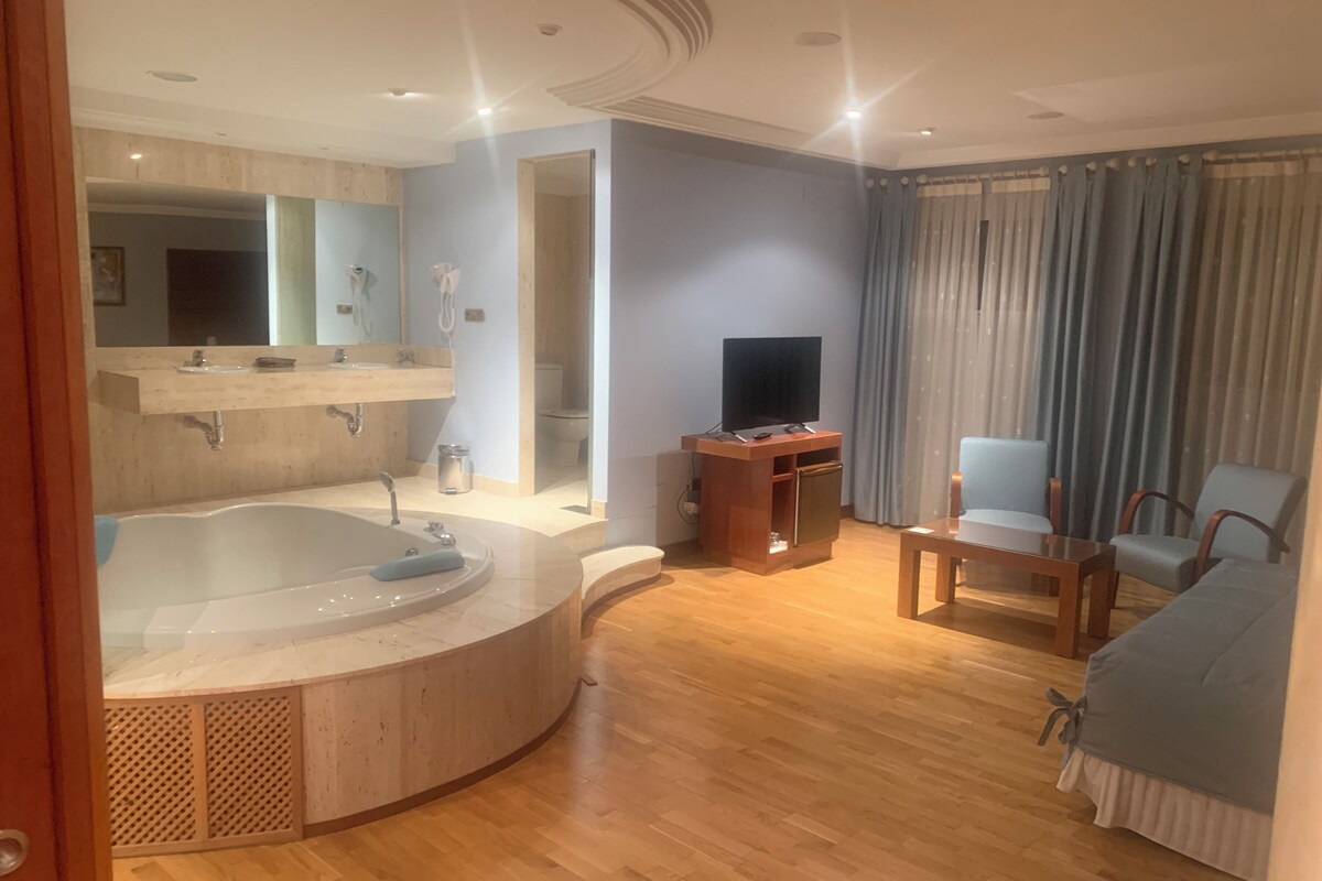A modern bathroom with a freestanding bathtub, a vanity with a mirror, and a toilet visible through an open doorway.