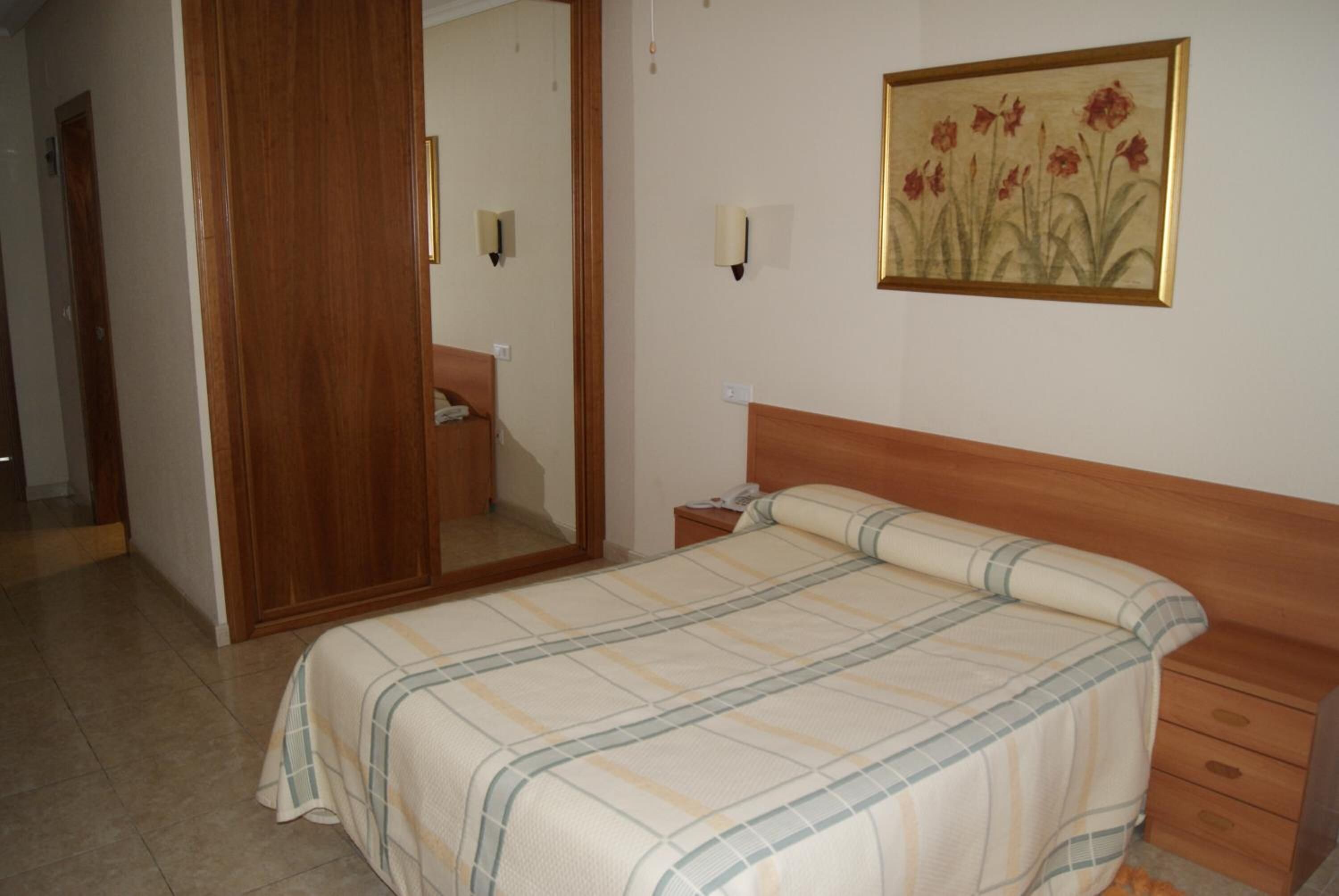 Een slaapkamer met een bed, een houten hoofdbord, een nachtkastje, een spiegel en een aan de muur hangend schilderij.