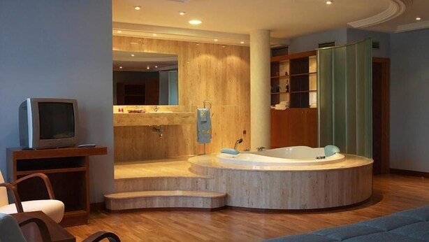 A modern bathroom with a freestanding bathtub, wooden vanity, and a television on a stand. - Hotel Alameda (Alba de Tormes)