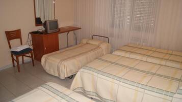 A room with two beds, a desk with a television, a chair, and a window with sheer curtains.