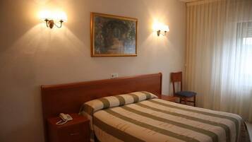 Une chambre d’hôtel avec un lit en bois, un téléphone sur la table de chevet et deux lampes fixées au mur.