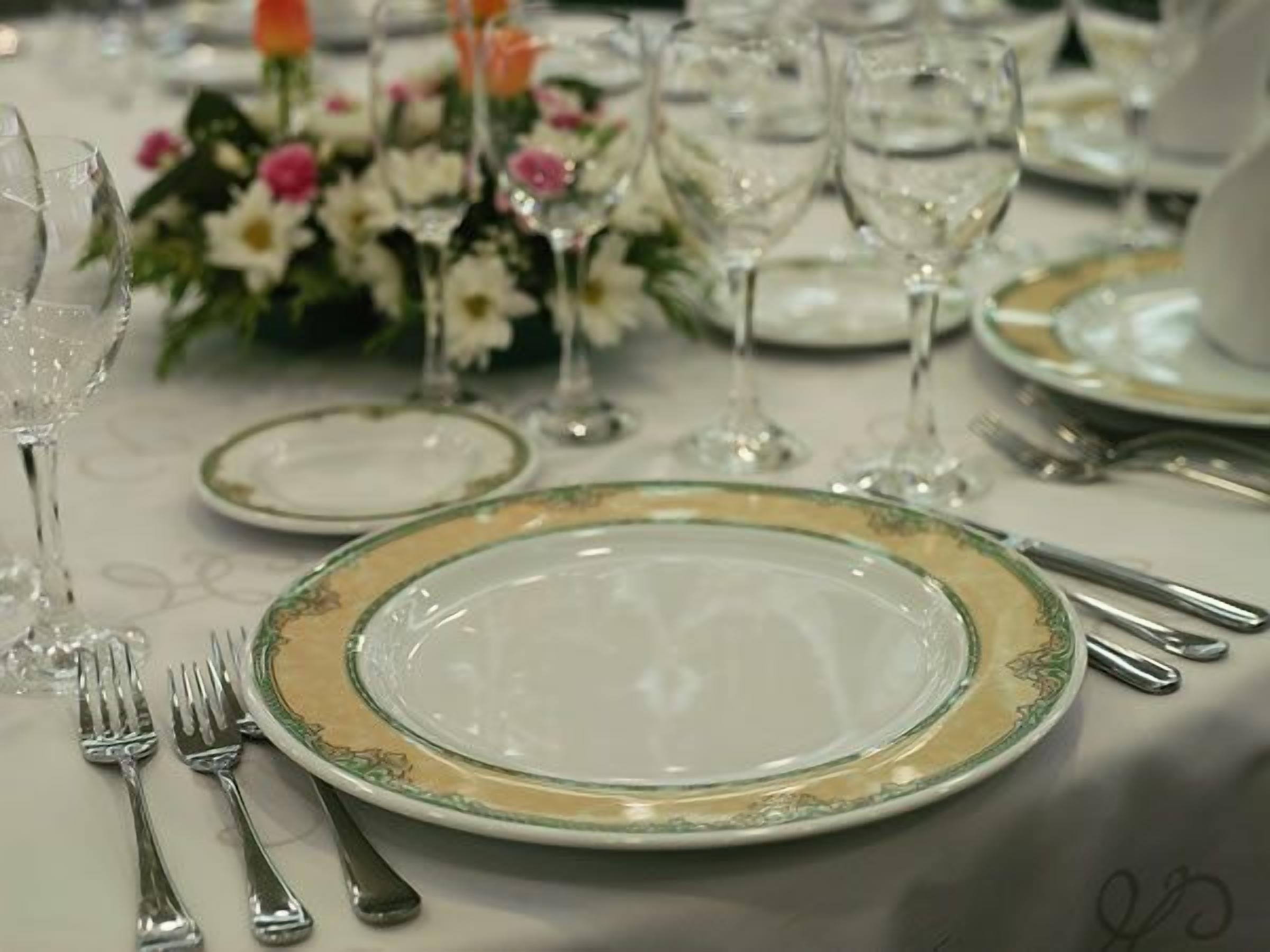 Una mesa servida con platos, cubiertos y vasos, con un centro de mesa floral.