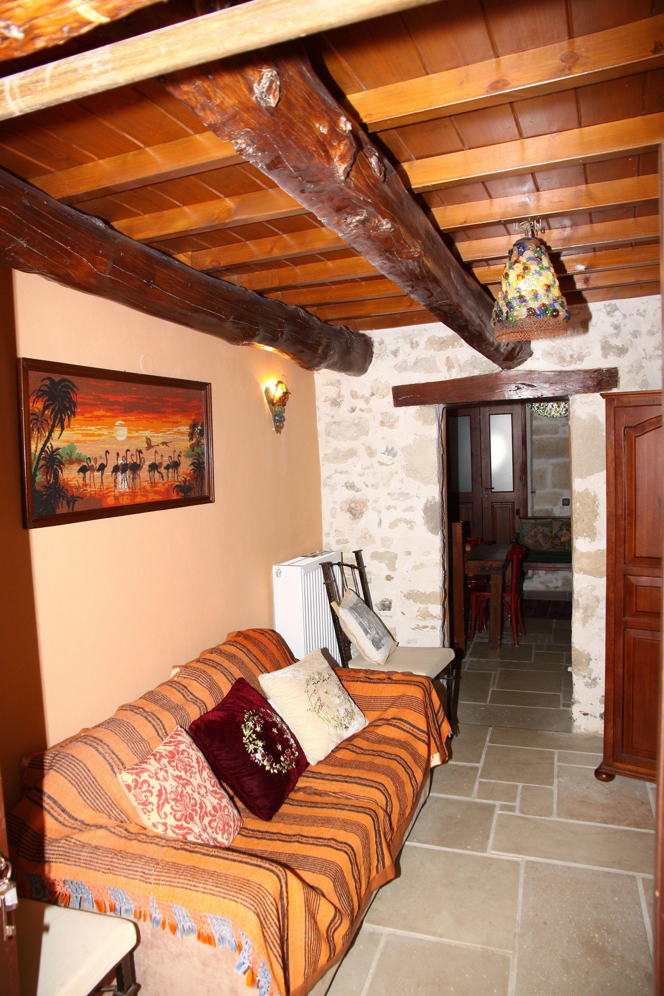 A cozy room with a wooden ceiling, a bed with patterned bedding, a painting on the wall, and a stone floor.