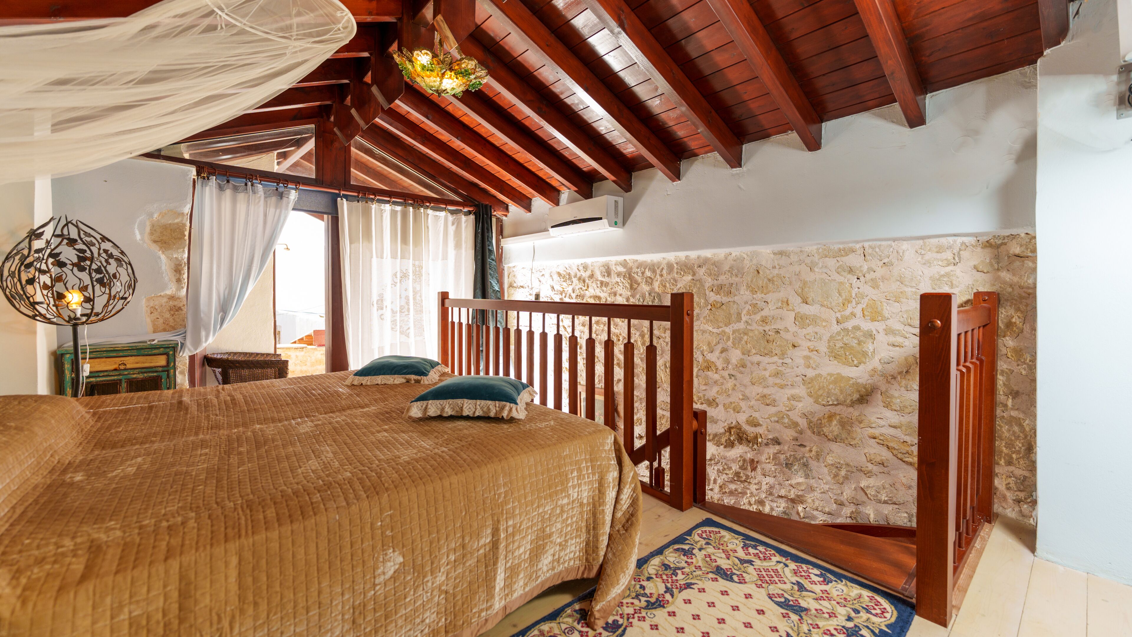 A bedroom with a wooden bed, a stone wall, and a wooden ceiling.