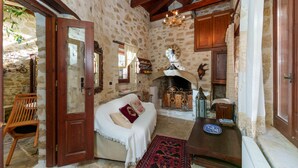 Una habitación rústica de piedra con una cama de madera, una chimenea y una mesa de madera con un plato.