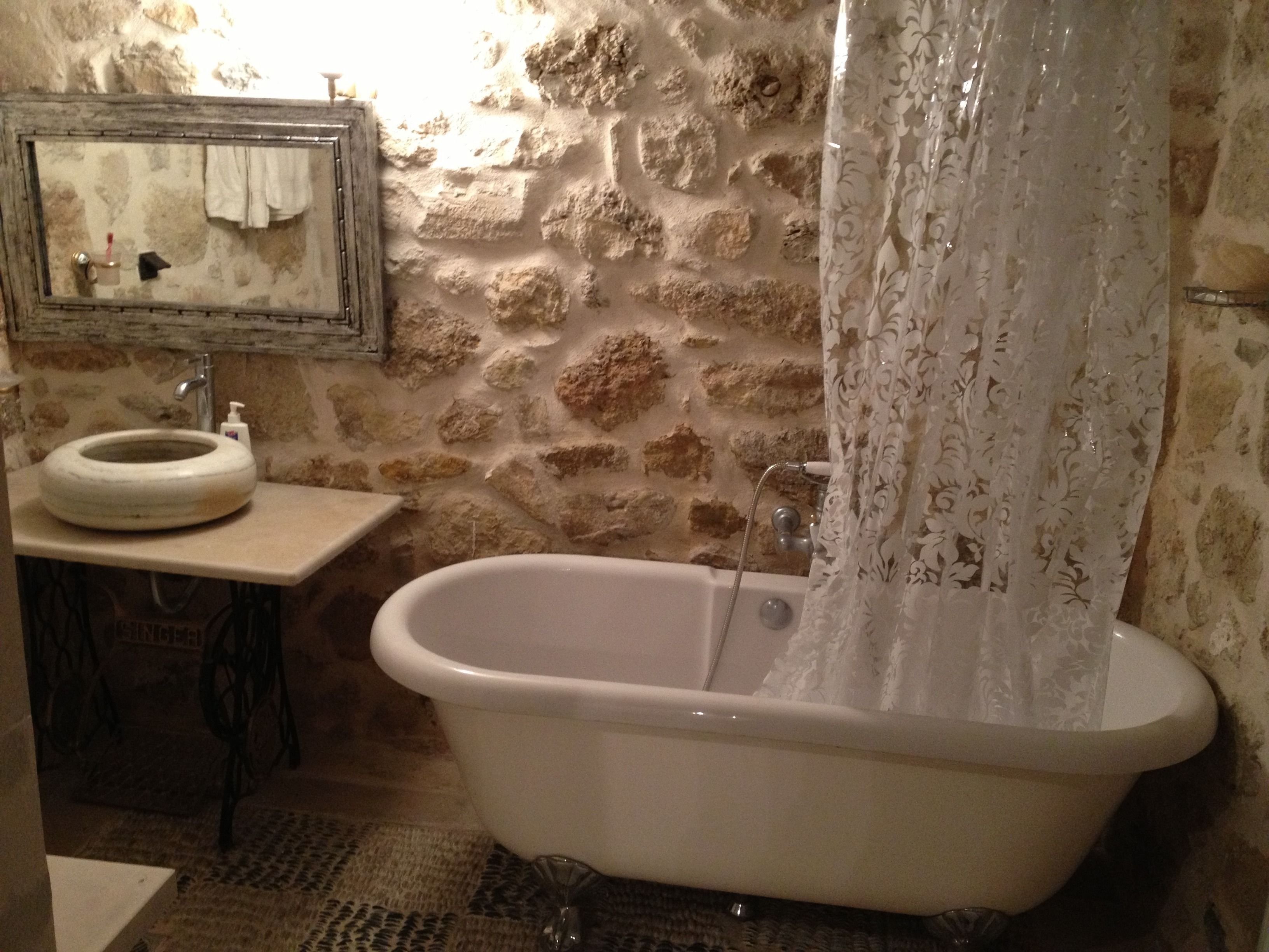A bathroom with a stone wall, a sink with a soap dispenser, and a bathtub with a shower curtain.