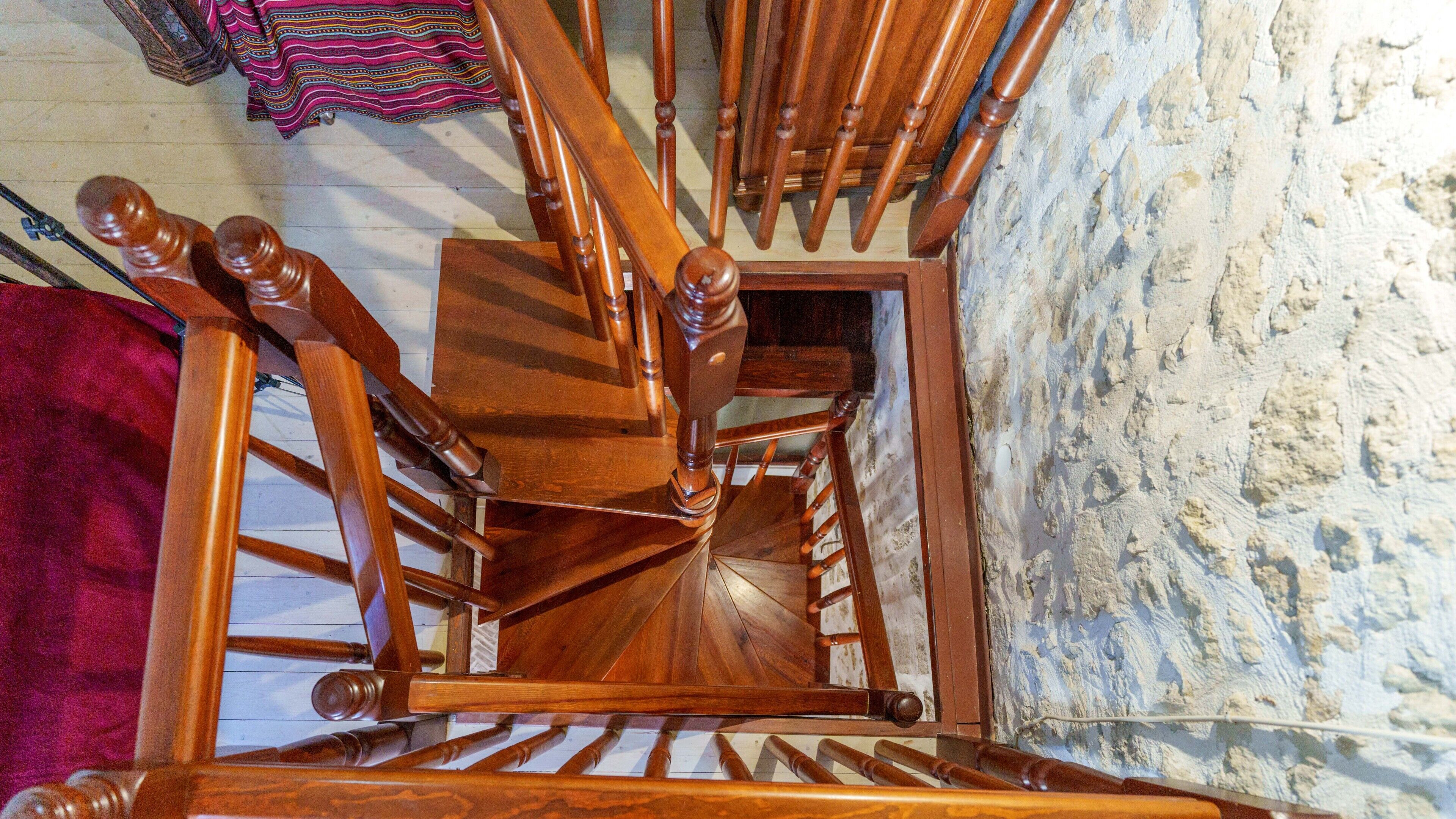 A wooden spiral staircase with a handrail, leading to an upper floor.