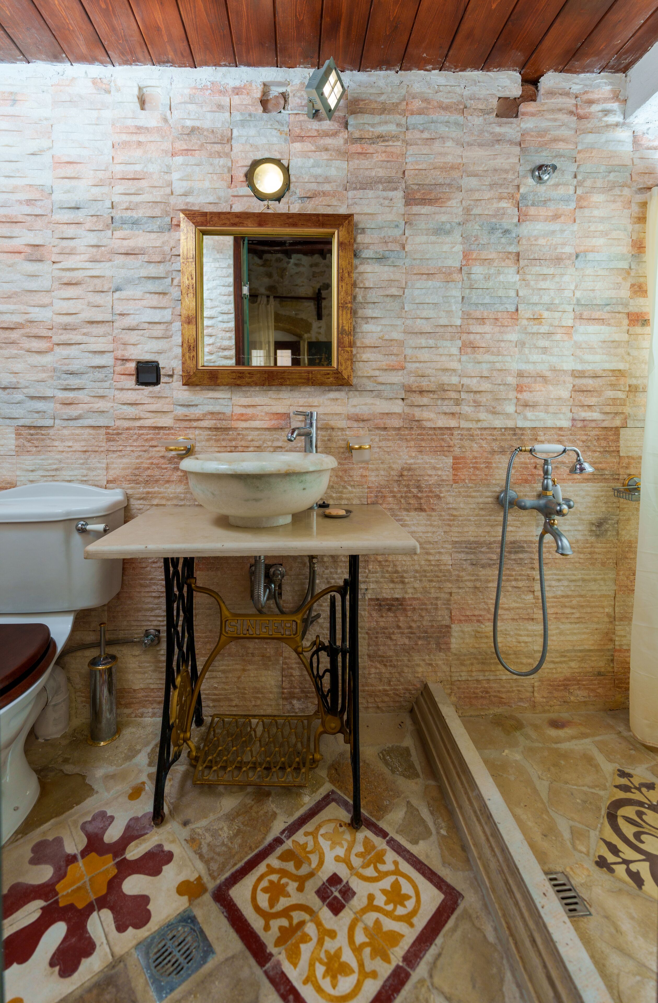 Een badkamer met een stenen muur, een houten plafond, een wastafel, toilet en douche.