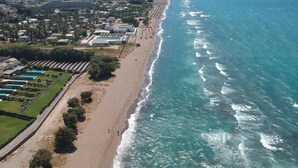 Vista aérea de una zona costera con playa, carretera y una hilera de edificios con piscina.